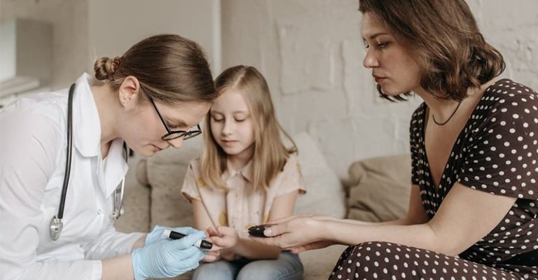 一名醫師與一名女子正在測量一個女孩的血糖。