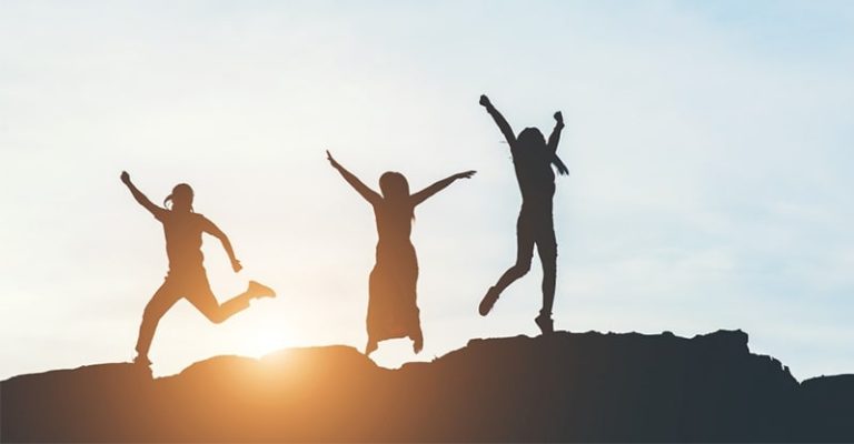 三個人在夕陽下的山頂上跳躍，氛圍充滿自由與喜悅。