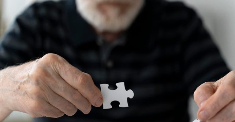 老人專注地拼拼圖，雙手握住拼圖塊，顯示出解謎過程中的專注力，這樣的活動將有助於預防失智症。