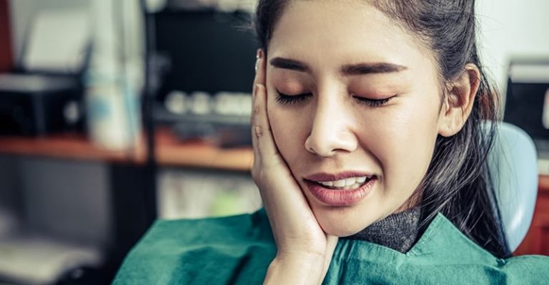一位女子在牙科診所捂著臉頰,表現出敏感性牙齒或牙痛的症狀。