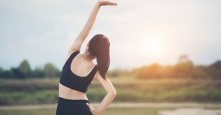 一位穿著運動服的女性正在戶外進行伸展運動，背景為美麗的自然景色和日落，展現了健康與活力的生活方式。