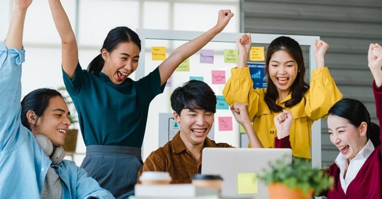 一群年輕上班族在辦公室裡開心慶祝成功,背景有色彩豐富的便條紙,展示了團隊合作和項目成功的情境。