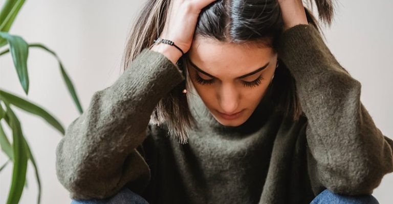 一位年輕女子坐著，低頭雙手抱住頭部，顯示出焦躁不安的情緒。