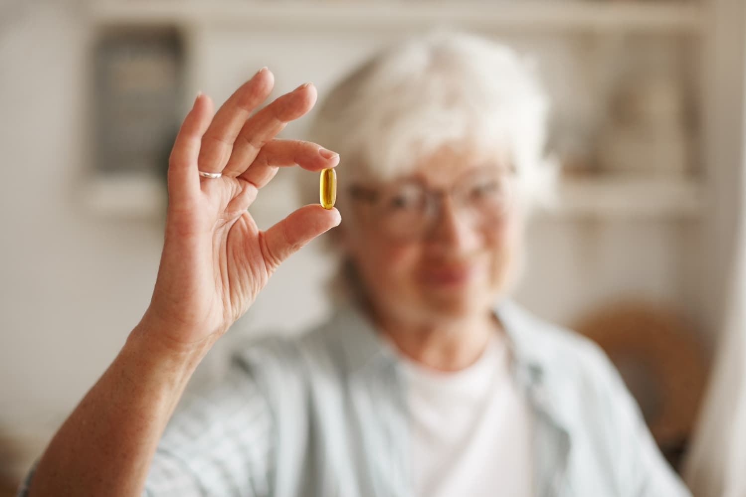 一名年長女子手持一顆魚油膠囊,展示 Omega-3 脂肪酸保健品的健康益處。