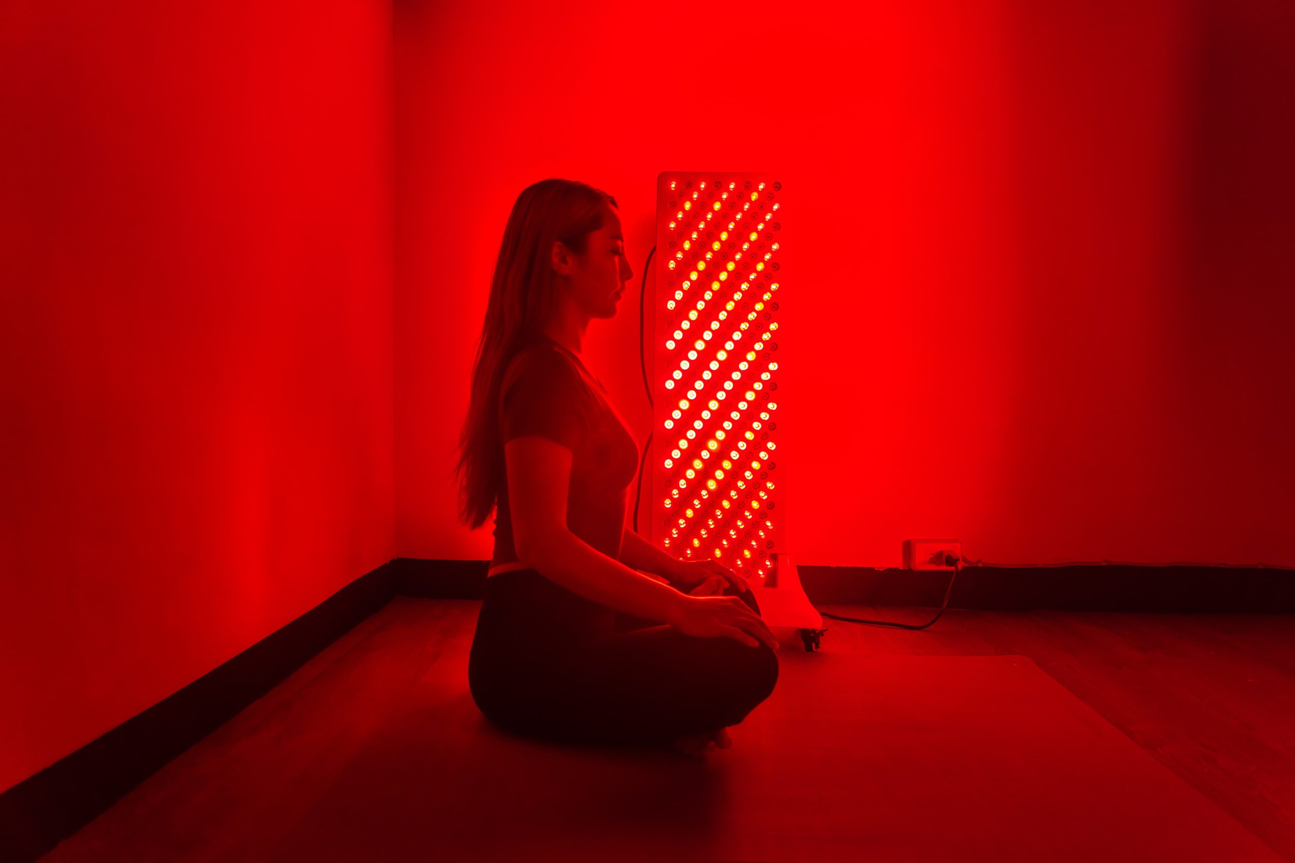 一名女子坐在紅光儀前冥想，享受溫暖的光照時光與居家放鬆氛圍。