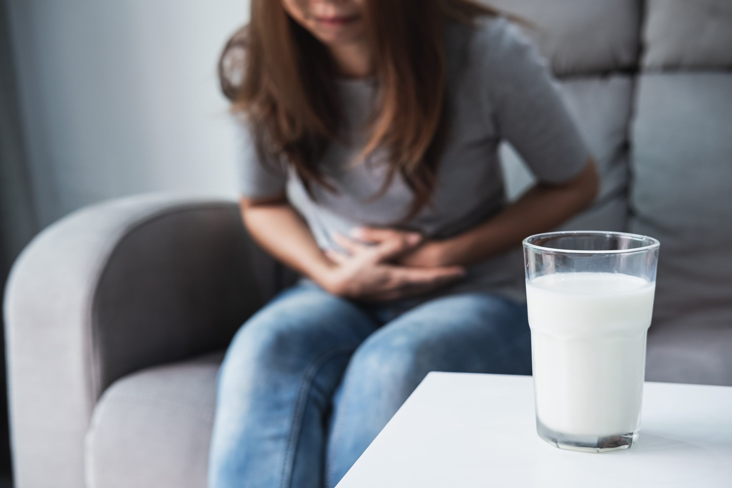 一名坐在沙發上的女子因乳糖不耐症感到腹部不適,面前桌子上擺放著一杯泡好的乳清蛋白。