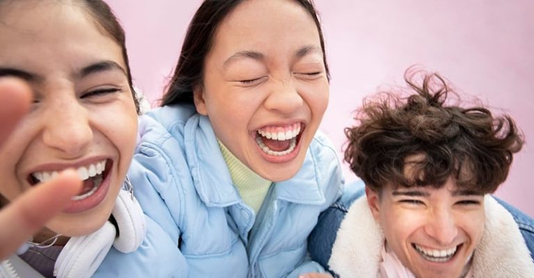 三位年輕人穿著冬季外套，開心大笑並享受著彼此的陪伴。這群青少年露出燦爛笑容，傳遞出快樂和友誼的氛圍。