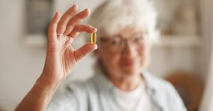 一名年長女子手持一顆魚油膠囊，展示 Omega-3 脂肪酸保健品的健康益處。