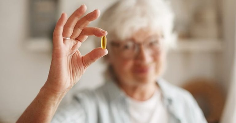 一名年長女子手持一顆魚油膠囊，展示 Omega-3 脂肪酸保健品的健康益處。