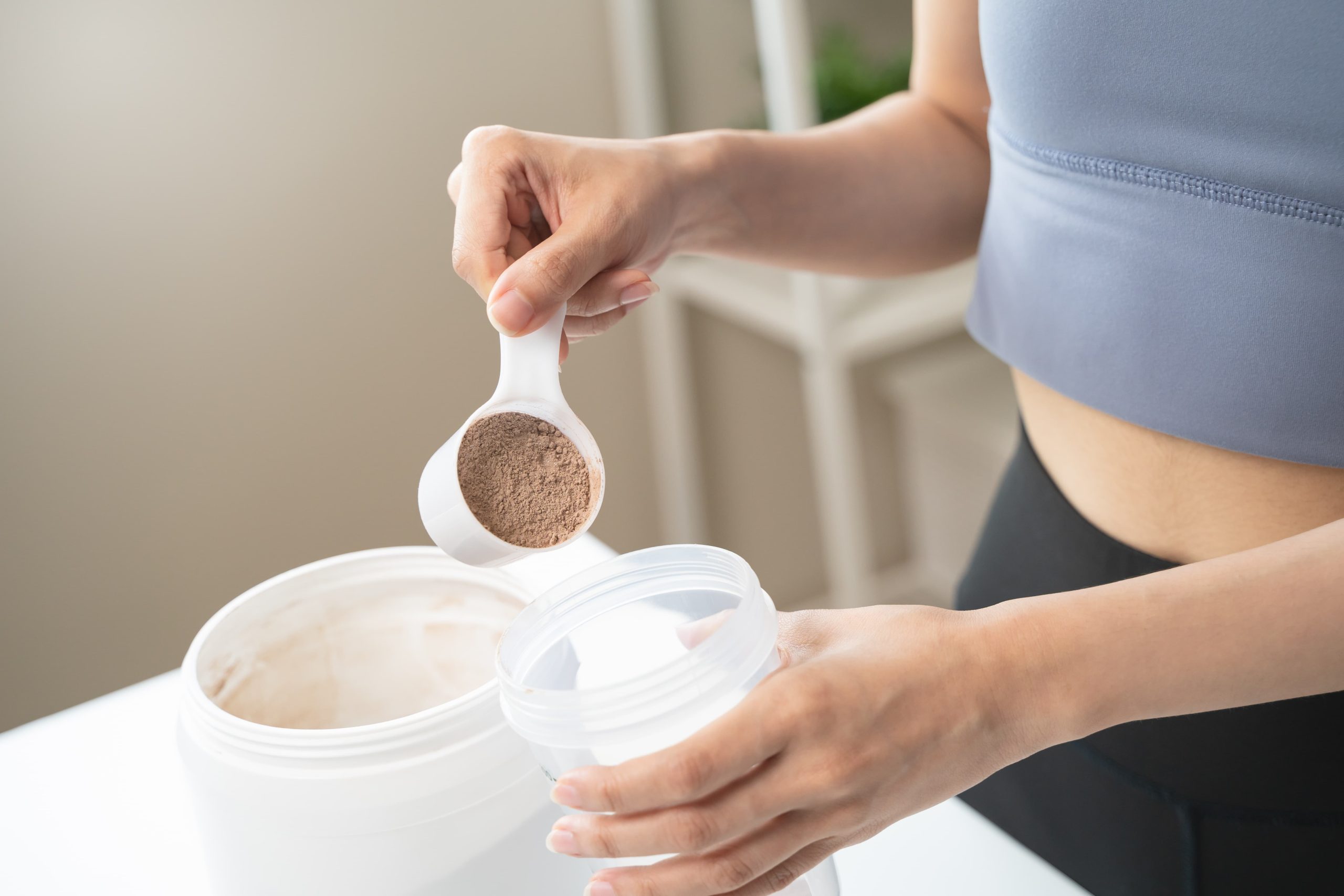 一名女子正在倒入乳清蛋白粉到搖搖杯中,準備補充運動後所需的蛋白質。
