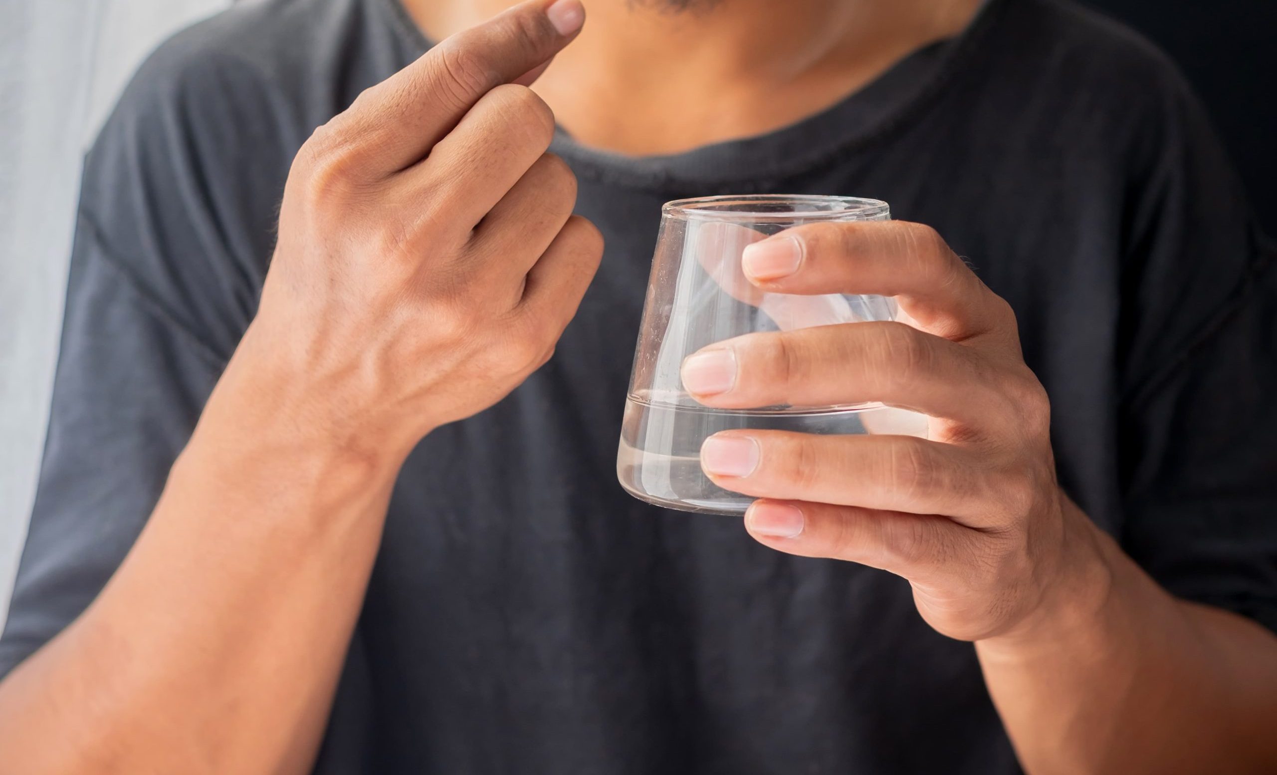 一名男子手持玻璃杯喝水,準備服用藍綠藻保健品。