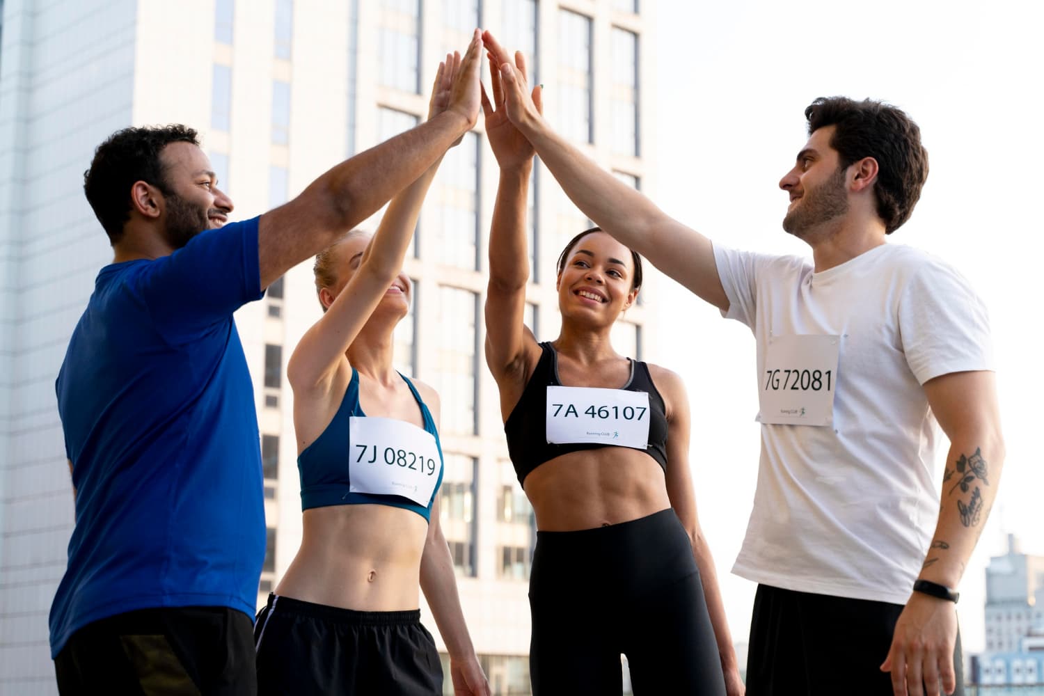 四位大學生運動員在比賽後高舉雙手擊掌慶祝,身穿號碼布,背景為城市高樓,展現團隊合作與運動精神。