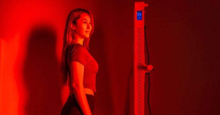 一名女子站立接受全身紅光療法照射,使用紅光儀促進血液循環與細胞修復,用於運動後肌肉恢復。