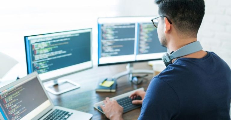 一位軟體工程師在現代辦公桌前操作多螢幕電腦,專注撰寫程式碼與開發系統。