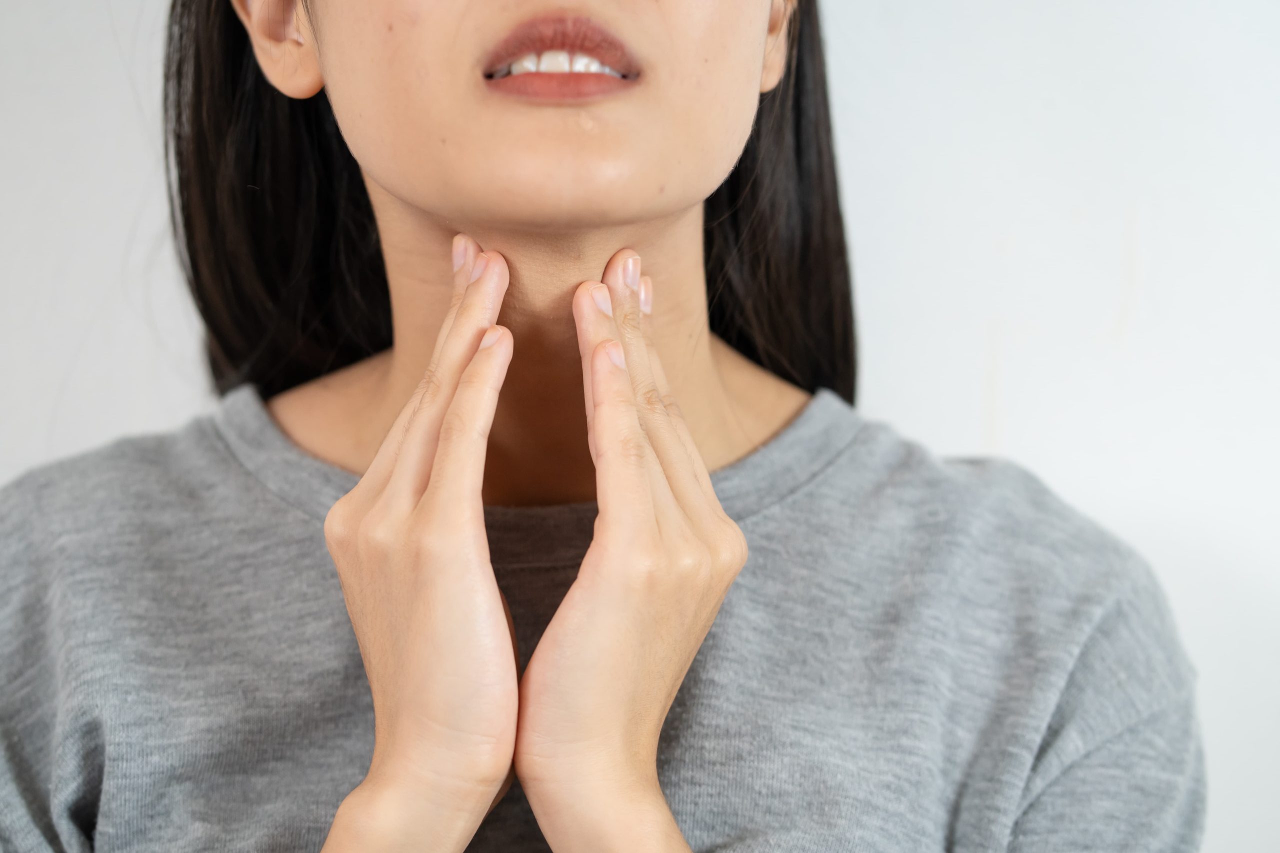 一名女子雙手輕按喉嚨處，表情略顯不適，示意聲帶不適或喉嚨痛，用於說明聲音疲勞、聲帶保養或喉嚨問題相關主題。