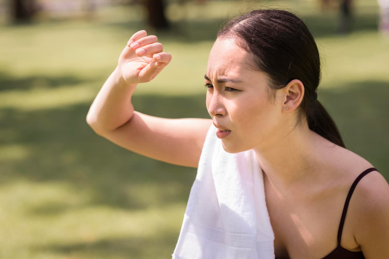 一名女子在烈日下遮陽皺眉,身上掛著毛巾,表情顯露不適,呈現炎炎夏日容易中暑的情境。