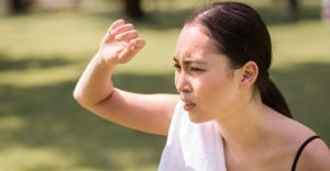 一名女子在烈日下遮陽皺眉，身上掛著毛巾，表情顯露不適，呈現炎炎夏日容易中暑的情境。
