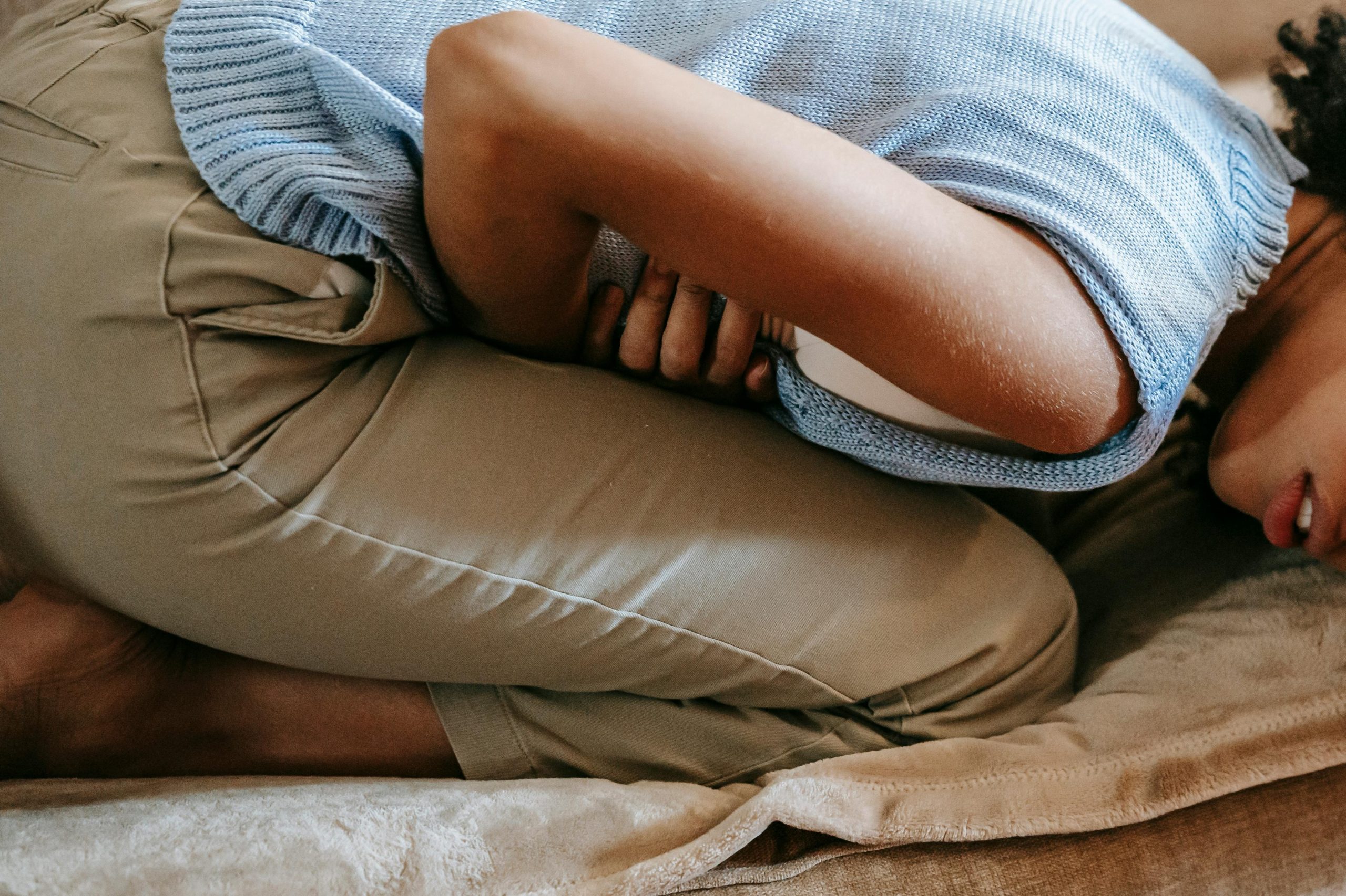 一名女子抱著肚子蜷縮在沙發上,表情痛苦,顯示生理痛的困擾。