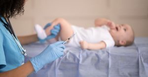 一位醫護人員正準備為嬰兒施打疫苗，以預防百日咳，嬰兒躺在診療台上。